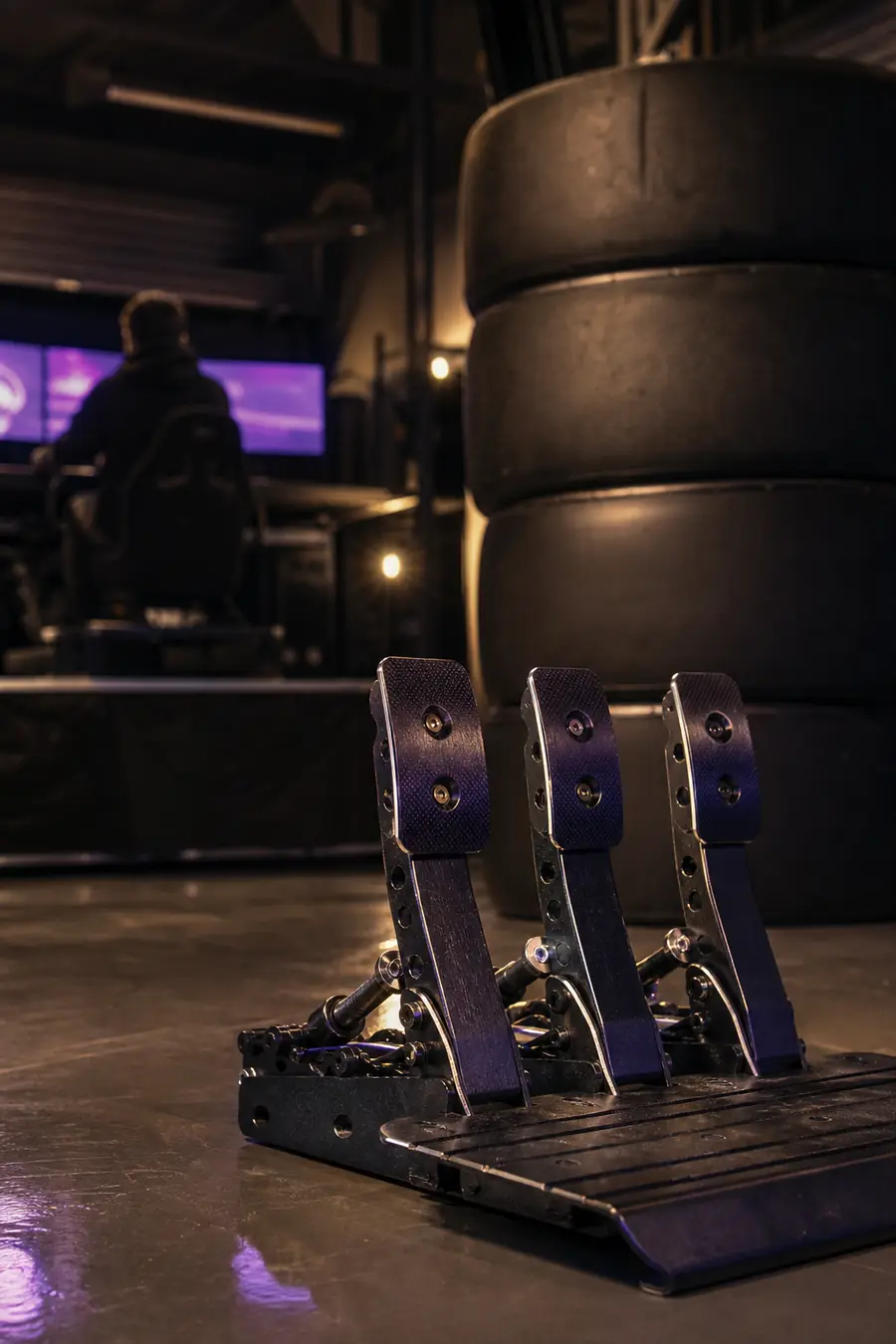 Racing tyres stacked in a garage behind a set of sim pedals.