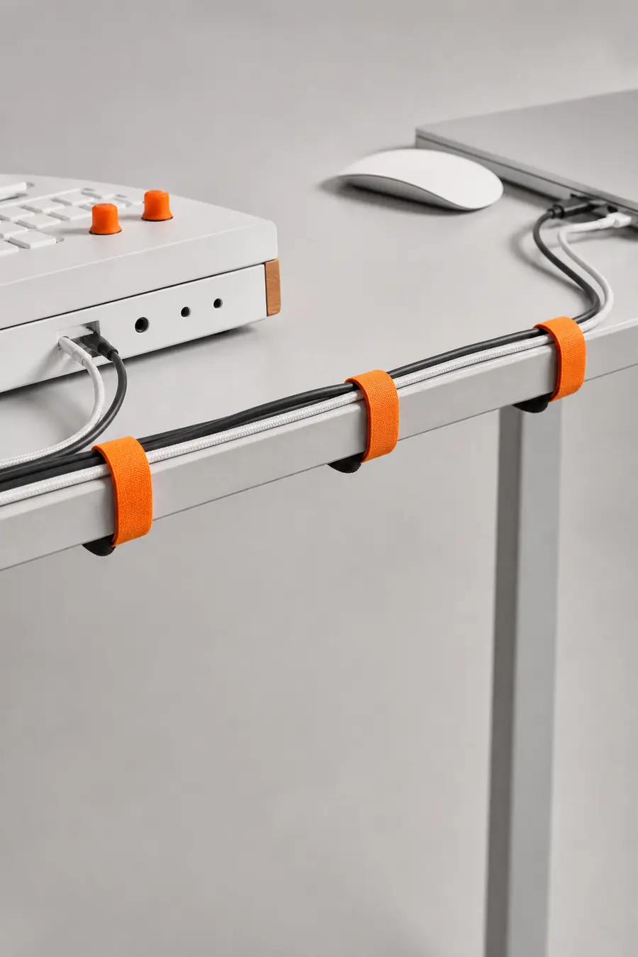 A tidy cable run held by orange ties along a light grey desk.